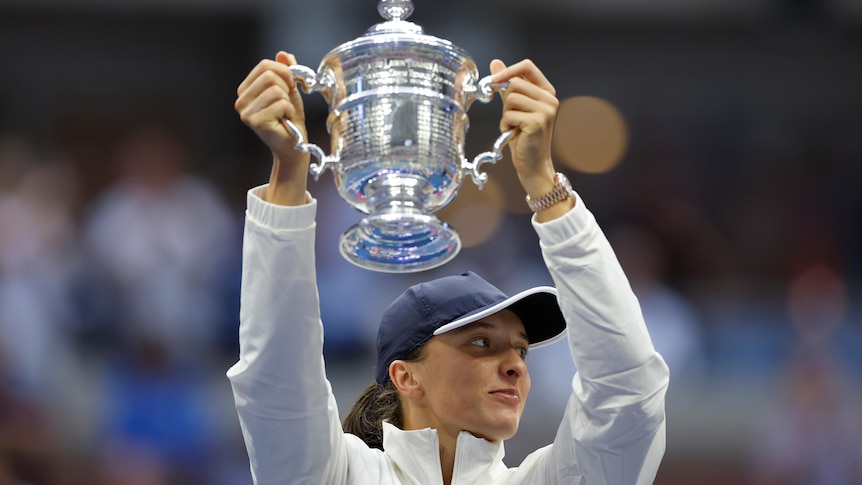 Iga Świątek holds the US Open trophy above her head.