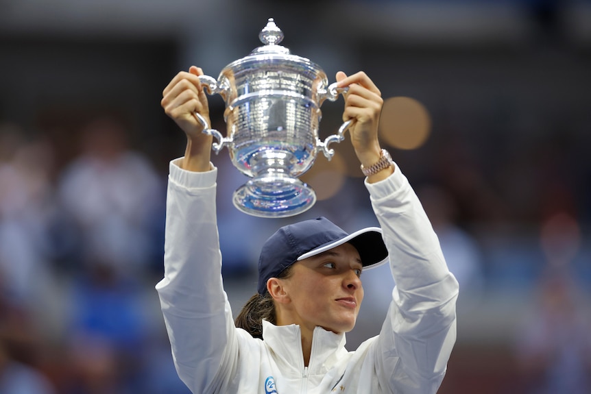 Iga Świątek holds the US Open trophy above her head.