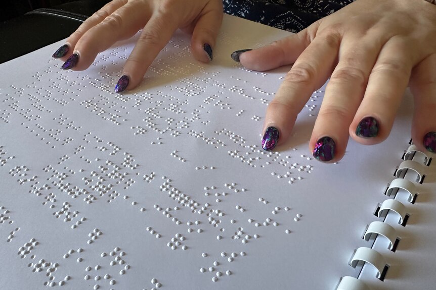Two hands feel raised braille markings on a white page. 