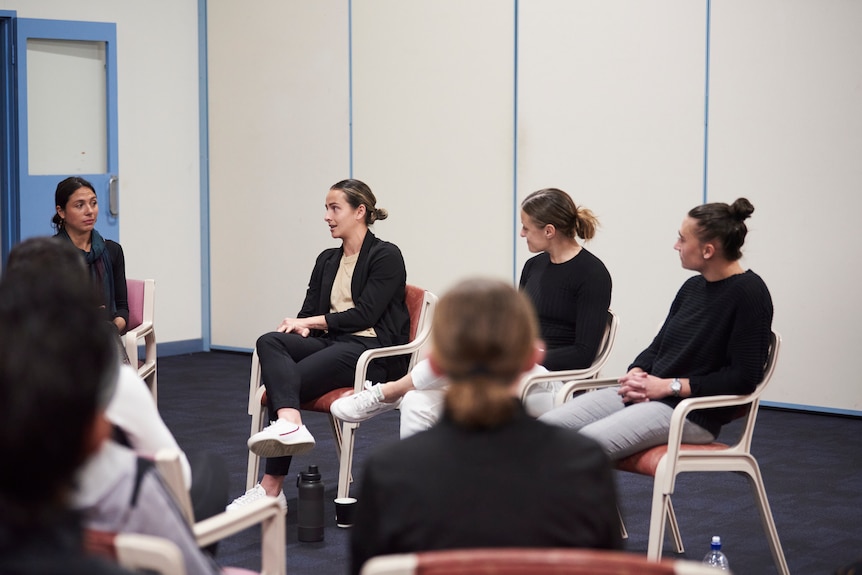 A panel of women seated indoors chat. 