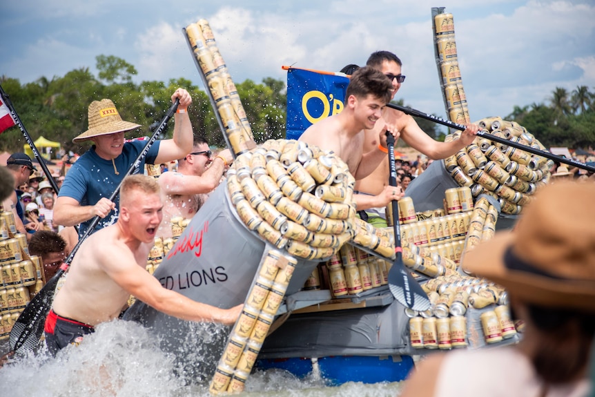 Four men start paddling on a boat made of cans in water at the beach 