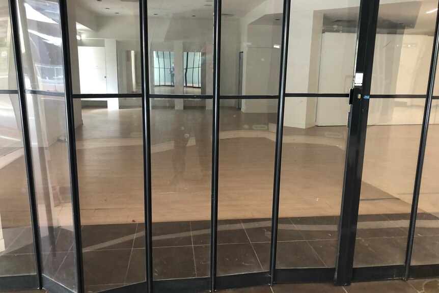 A retractable glass door pulled closed on a vacant shop in a mall.