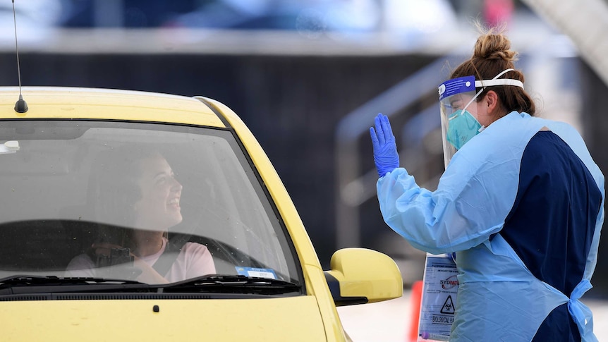A woman in a yellow car and a COVID testing woman smile at each other