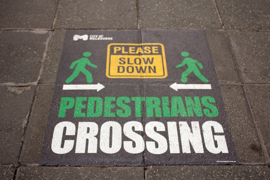 A sign on the pavement reading "please slow down, pedestrians crossing".