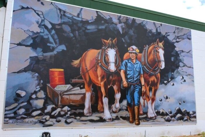 a painted mural showing old-fashioned horse-drawn mining machinery and a man leading the horses