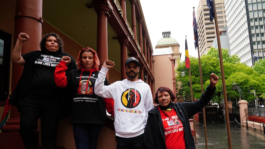 four people wearing clothes with slogans that call for justice stand with their arms raised