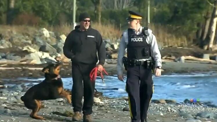 Mike Johns and his dog Taz walk along the beach with a police officer.