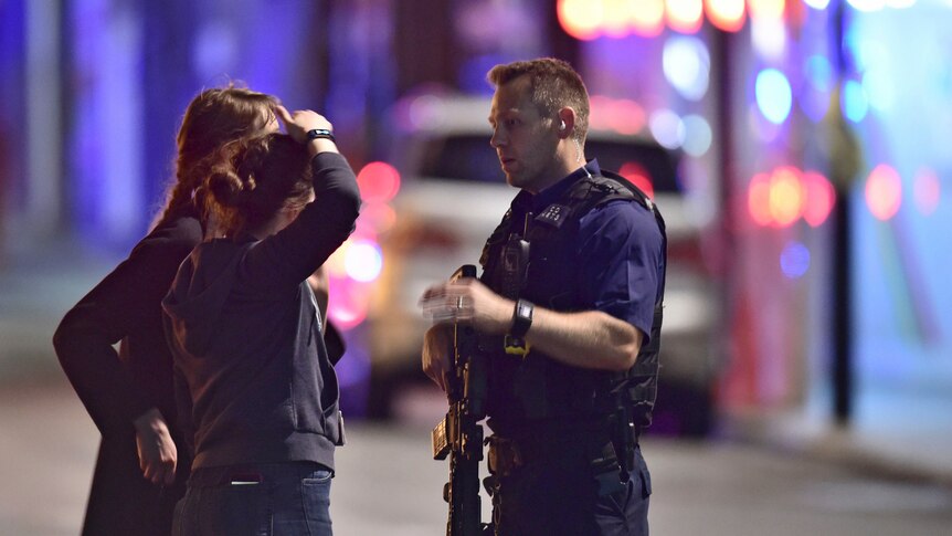 An armed Policeman talks to members of the public outside London Bridge Hospital.