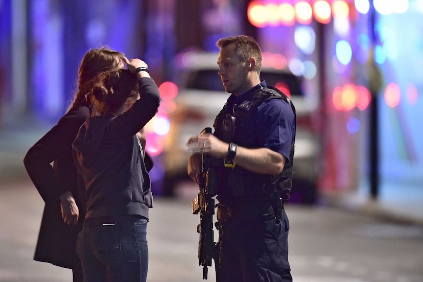 An armed Policeman talks to members of the public outside London Bridge Hospital.