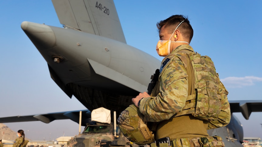 Australian soldiers wearing face masks stand on a military tarmac