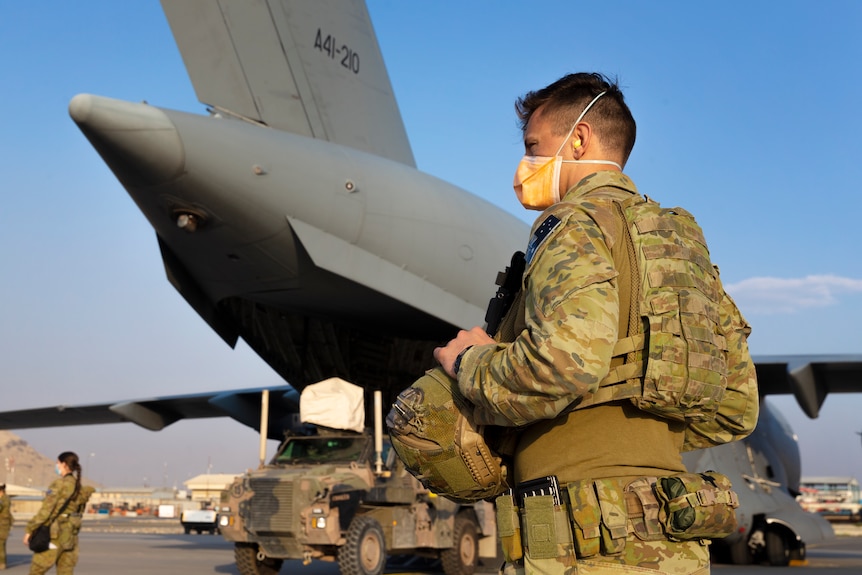 Australian soldiers wearing face masks stand on a military tarmac