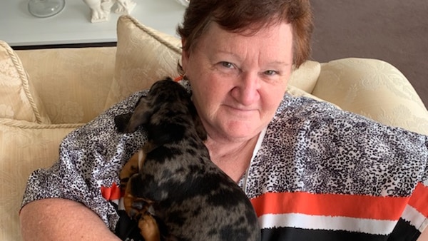 a woman sits on a couch cuddling a puppy