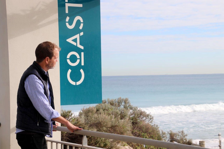 Port Beach's Coast restaurant owner Ian Hutchinson stands in front of a large Coast sign, looking over the ocean.