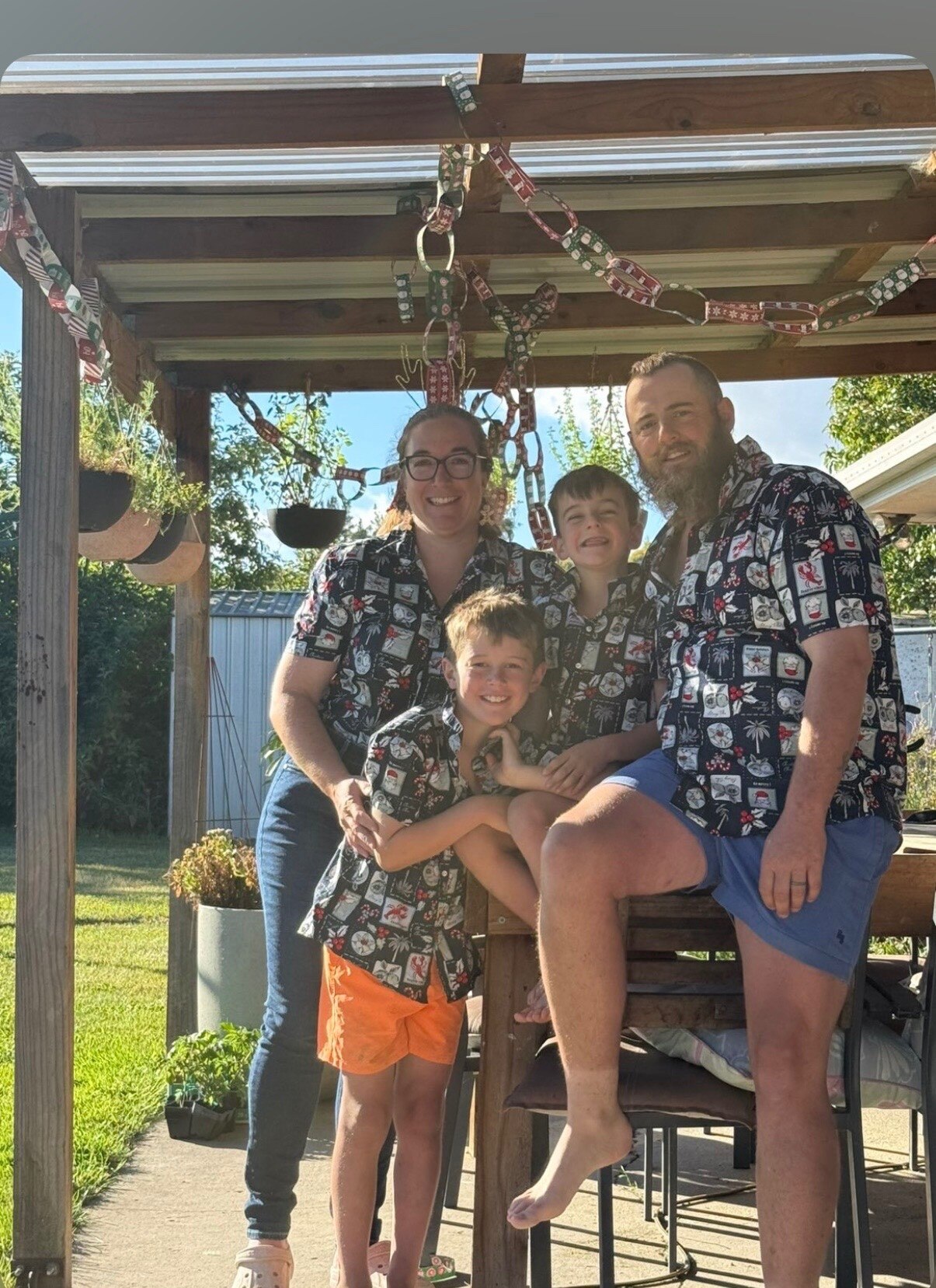 A woman posing with her husband and two young boys in matching shirts.