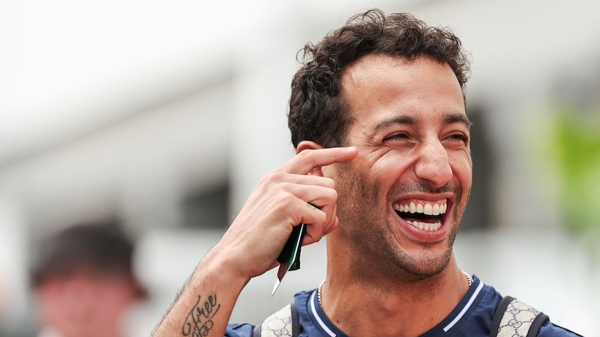 A man in a dark blue polo shirt, laughing and looking over his shoulder.