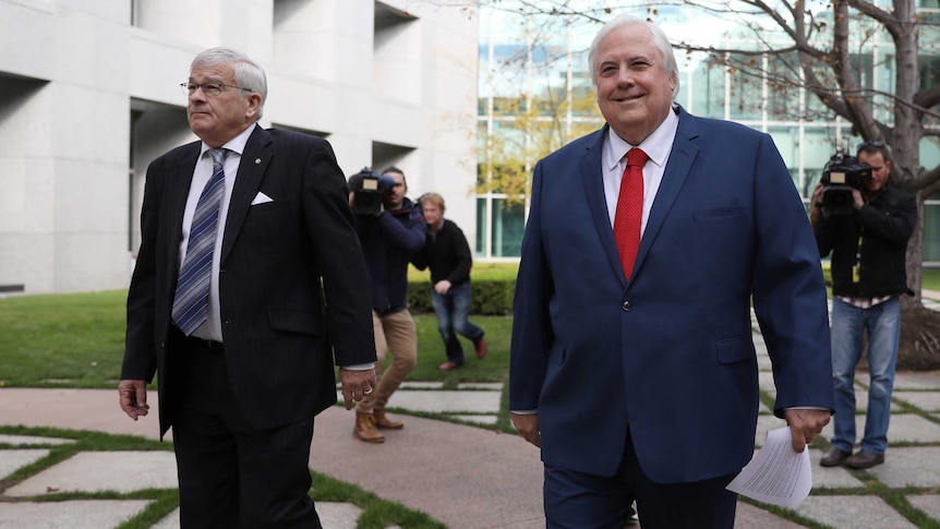 Brian Burston, in a black suit and patterned tie strolls next to Clive Palmer, in a red tie and blue suit.