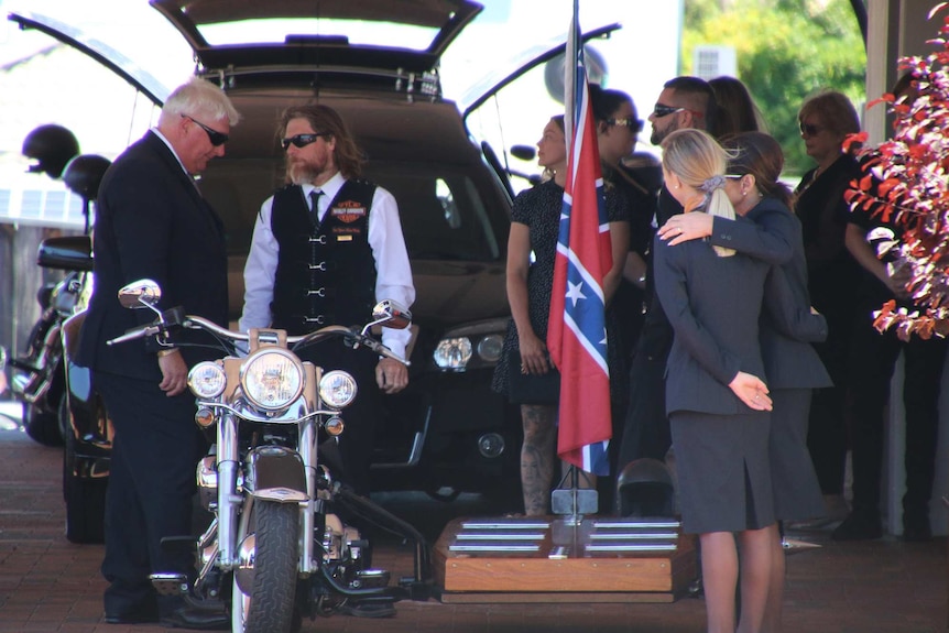 A motorbike in front of hearse at Nick Martin funeral. a blue and red confederate flag is flying.