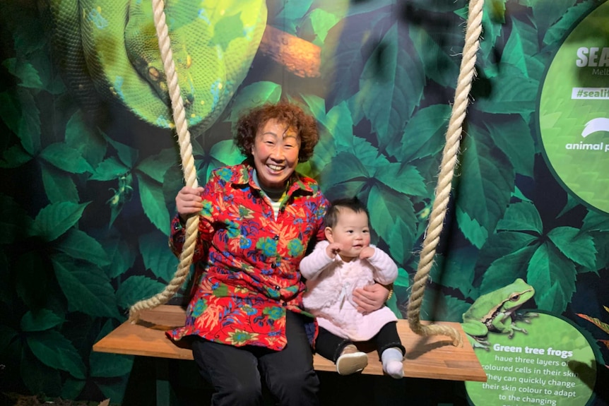 Lixia Wang with Emma Liu next to her on a swing.