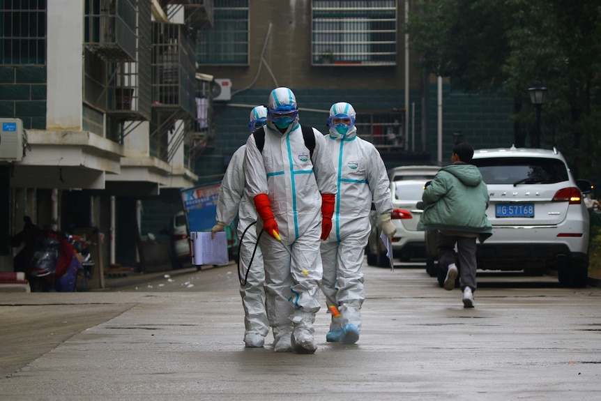 Three men in protective suits and masks  in a residential area, holding a wand attached to a pipe while a child passes by