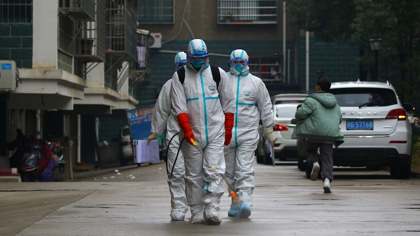 Three men in protective suits and masks  in a residential area, holding a wand attached to a pipe while a child passes by.