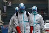 Three men in protective suits and masks  in a residential area, holding a wand attached to a pipe while a child passes by.