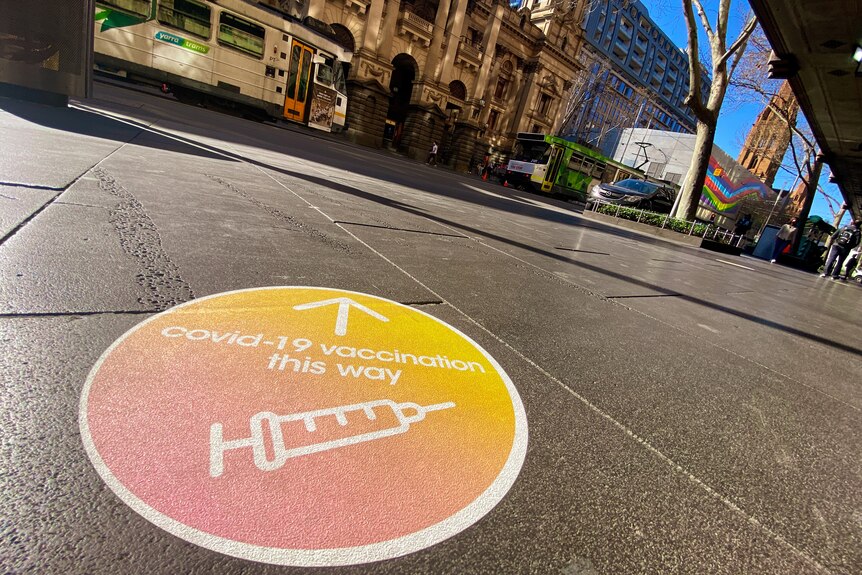 An orange sticker on pavement showing the direction to a vaccination clinic