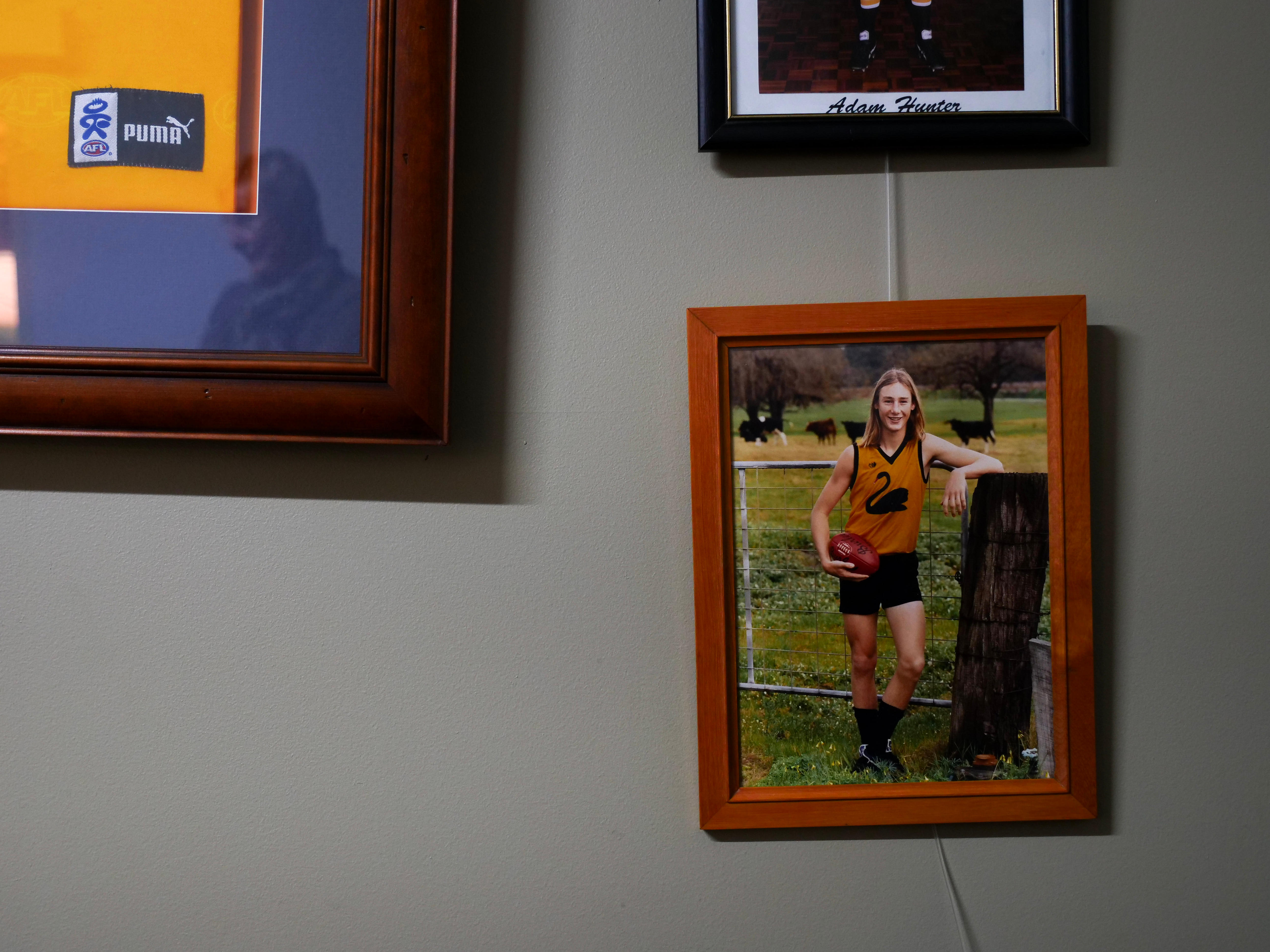 A photo of a young boy with long hair in a footy guernsey hangs on the wall