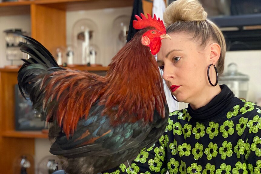 Natalie is sitting at a table working on a taxidermy chicken that is on the table in front of her. 