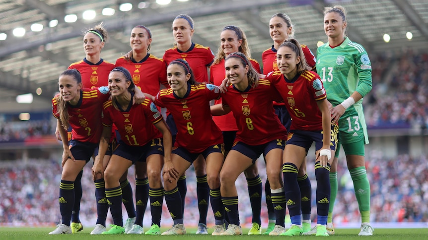 A soccer team wearing red, yellow and blue poses for a photo with a crowd behind them