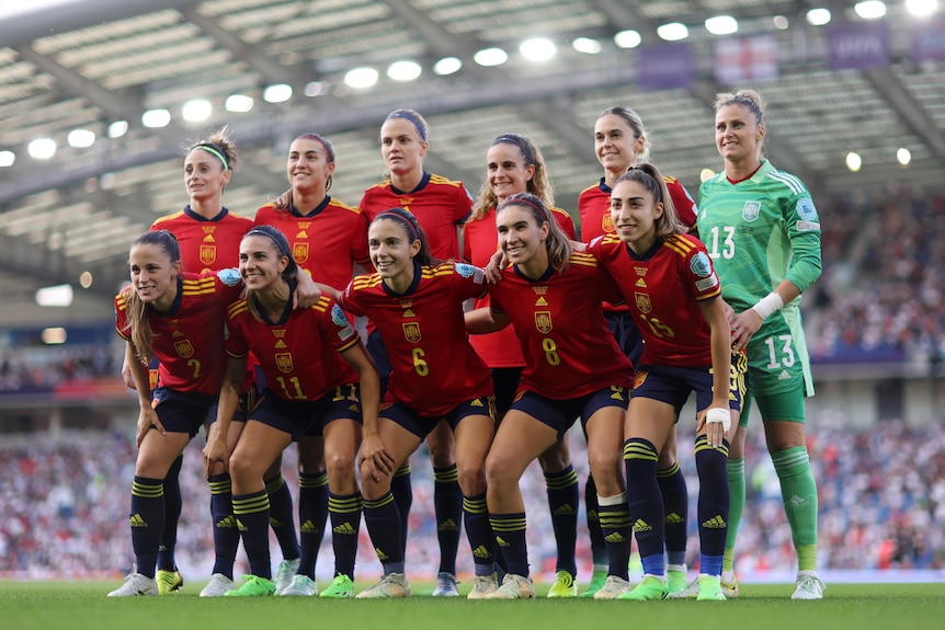 A soccer team wearing red, yellow and blue poses for a photo with a crowd behind them