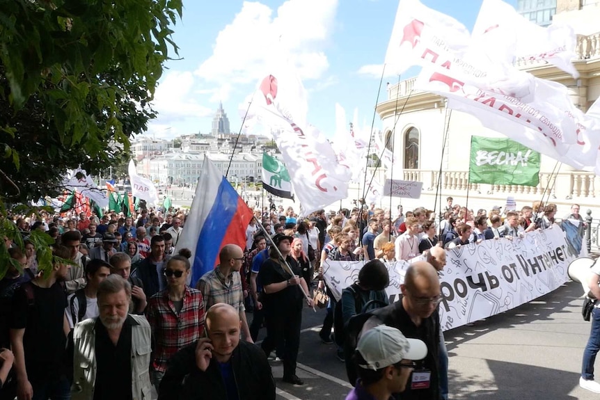 A large crowd carrying signs marches through the streets of Moscow.
