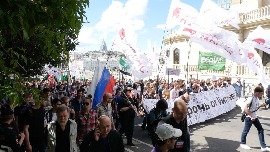 A large crowd carrying signs marches through the streets of Moscow.