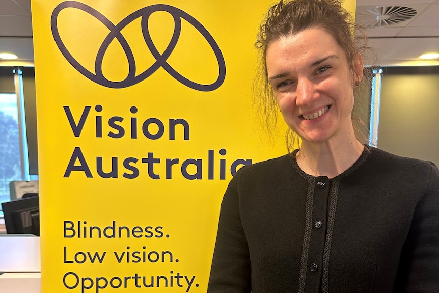 Vildana stands in front of a Vision Australia banner that reads "Blindness. Low vision. Opportunity."