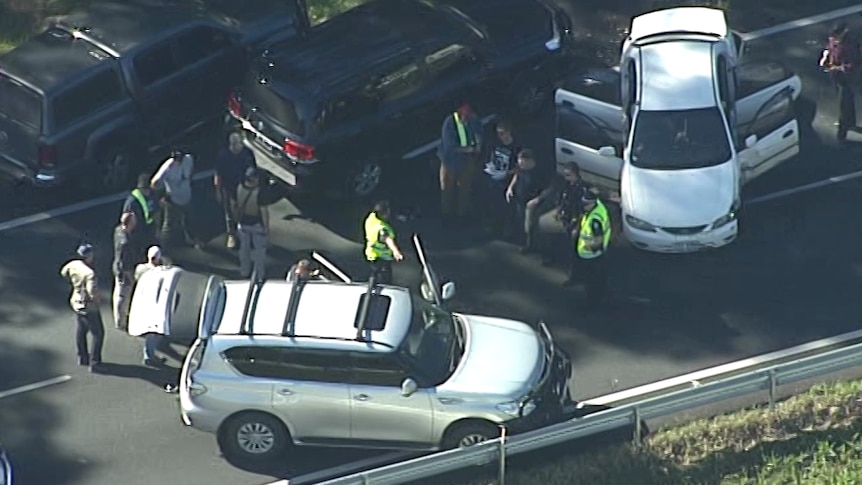 A dozen people including police officers in uniform stand around a number of cars blocking the Bruce Highway.