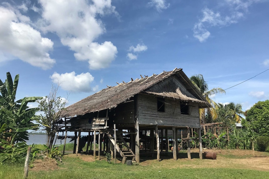 A wide view of a house built on stilts in a grassy area with water behind.