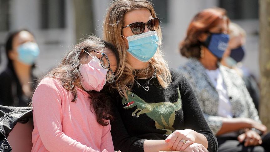 Une femme portant un masque est assise en commençant ahea avec sa fille appuyée sur elle.