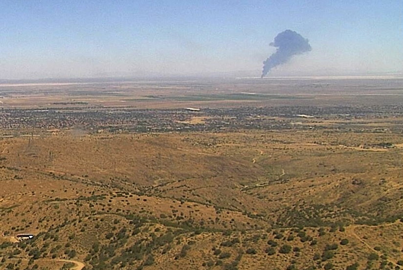 A yellow terrain with a plume of smoke rising in the far distance
