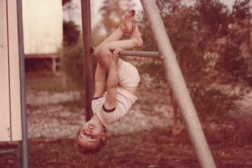 a young girl hangs upside down on a swing
