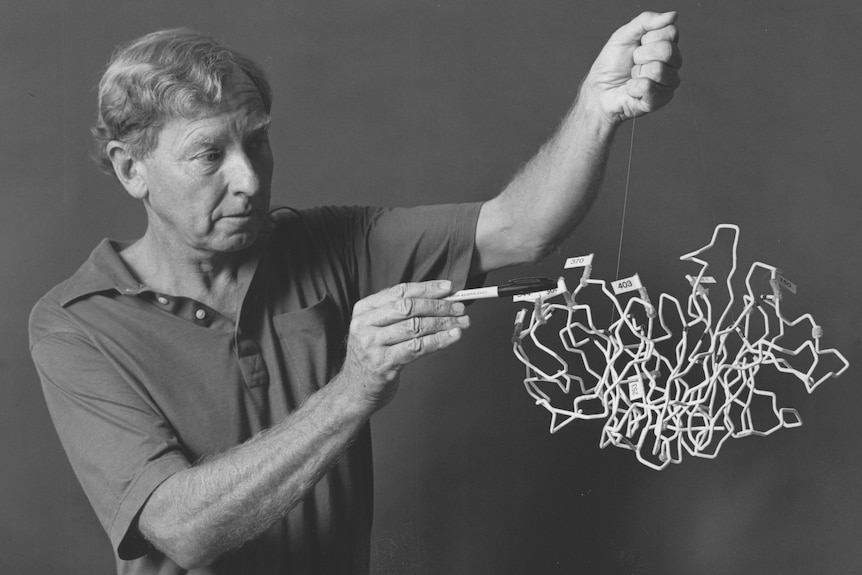 A black and white photo of a man with short hair wearing a polo shirt holding a scribbly looking crystal structure
