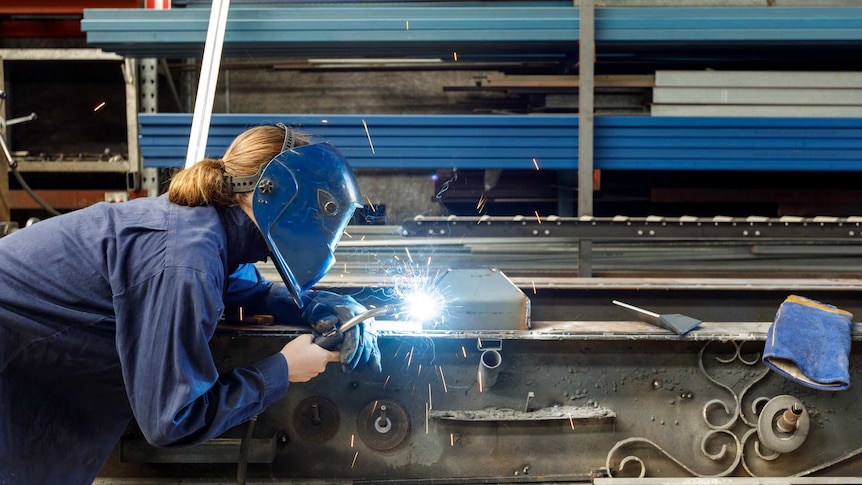 Young Female Welder Working In Factory Wearing Protective Safety Gear.