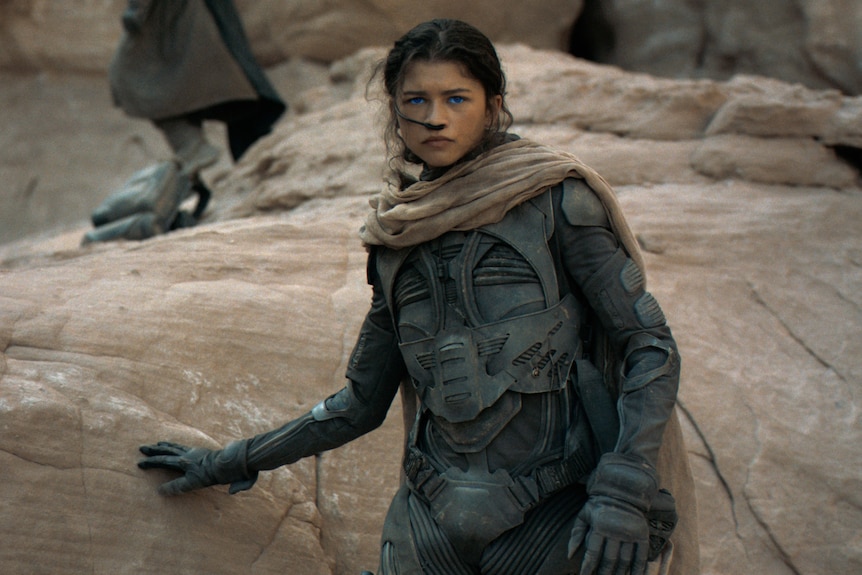 An African American woman in her 20s looks determined, standing with a palm pressed against a large rock