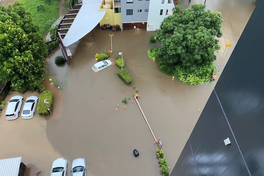 Flooding around an apartment building viewed from above, with cars underwater.