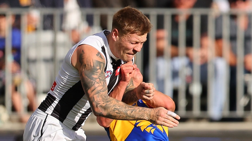 A Collingwood AFL player grimaces as he cannons into a West Coast player in mid-air.