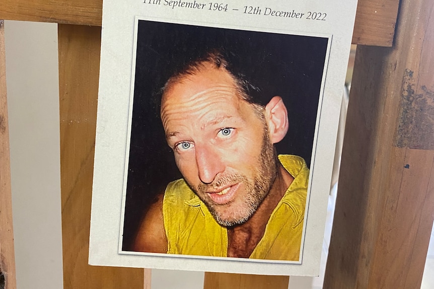 a poster hanging on a barrier that says 'in loving memory alan dare' with a photo of him wearing a yellow shirt