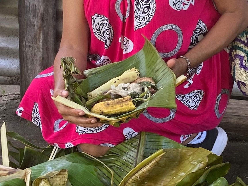 Woman sitting with food wrapped in a banana leaf. 