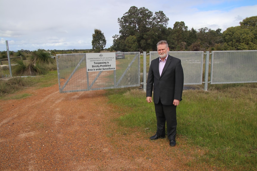 A man poses for a photo standing in front of a fence on Department of Defence land in Bullsbrook.