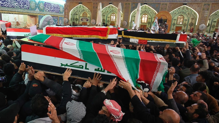 A large crowd carry two coffins with Iraqi flags on them