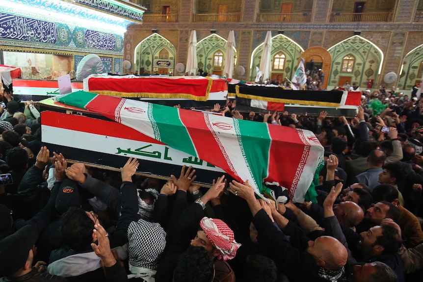A large crowd carry two coffins with Iraqi flags on them