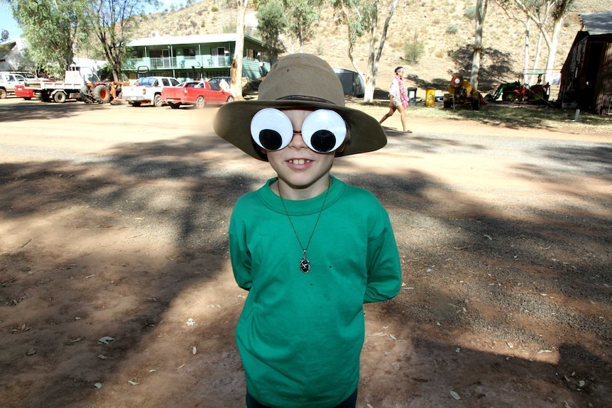 Boy stands wearing giant googly eyes and akubra-style hat.
