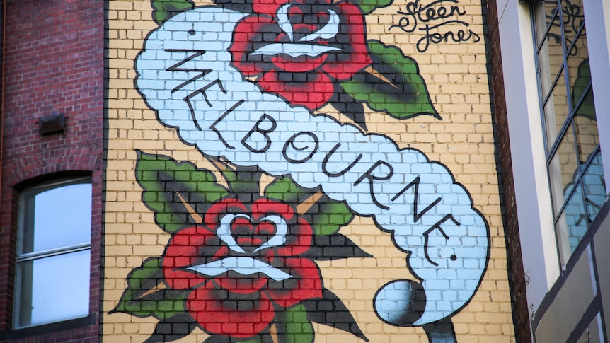 The word 'Melbourne' on a blue banner with red roses either side is painted on a brick wall in inner Melbourne.